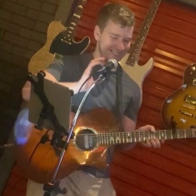 Bergen County singer and musician JP Nicks smiling at mic stand while playing guitar